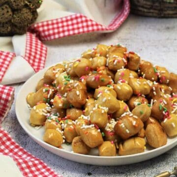 Traditional Sicilian pignolata covered with honey piled on serving plate next to spoon.