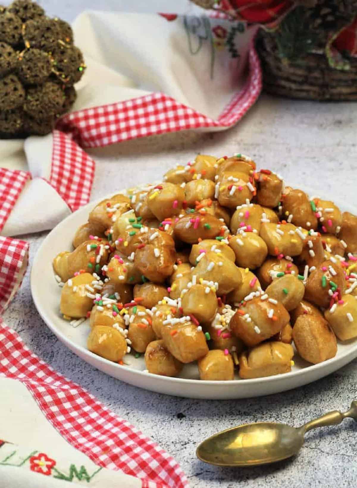 Traditional Sicilian pignolata covered with honey piled on serving plate next to spoon.