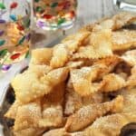 Chiacchiere di Carnevale, fried strips of sweet dough, piled on serving dish and covered with powdered sugar.