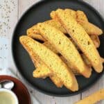 Anise biscotti piled on plate next to coffee cup.