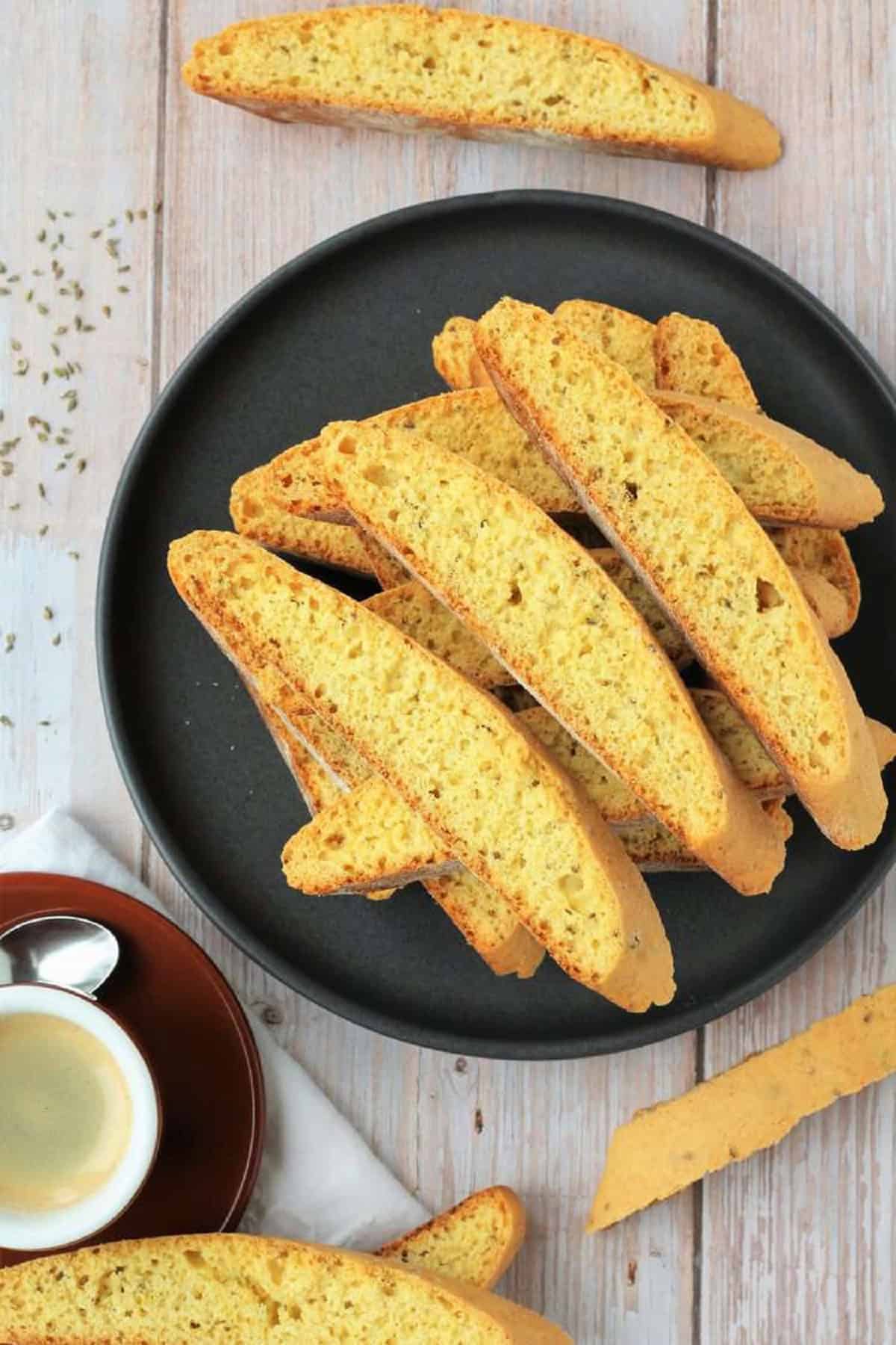 Anise biscotti piled on plate next to coffee cup.