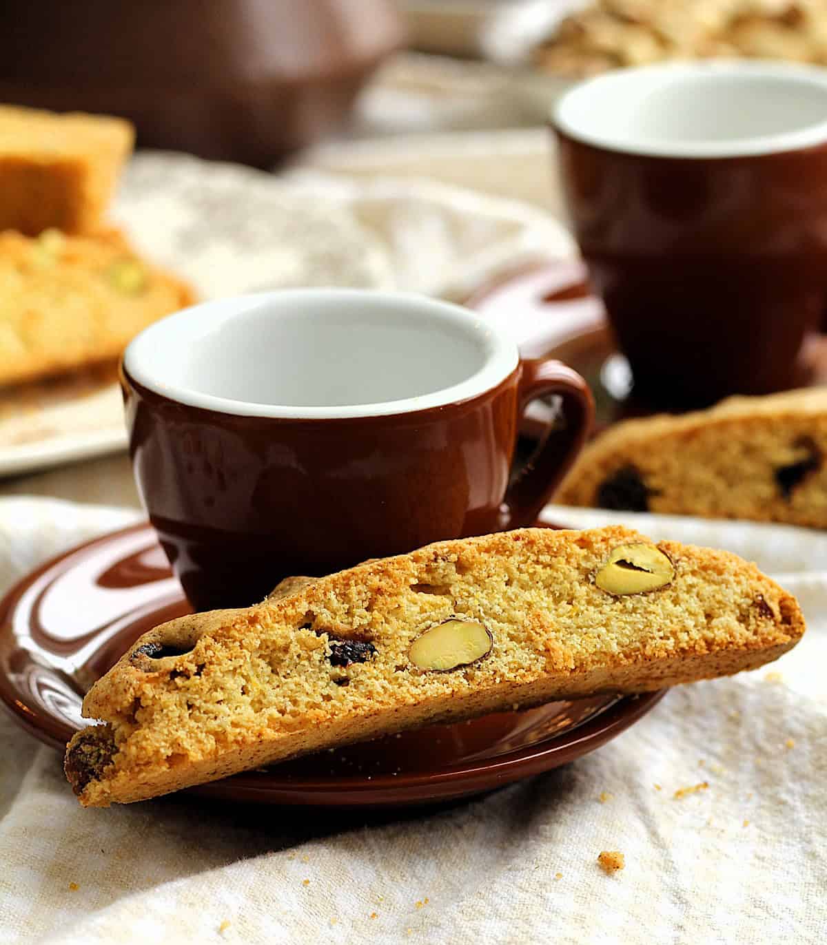 Cornmeal biscotti with cranberries and pistachio on coffee cup saucer.