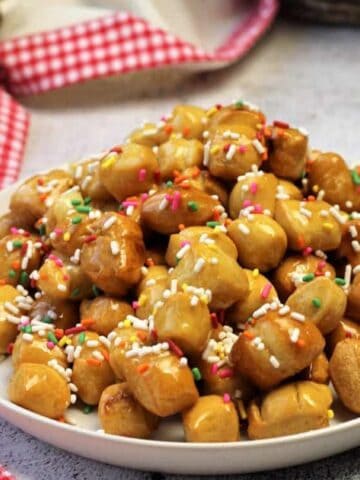 Traditional pignolata drenched in honey piled on plate.