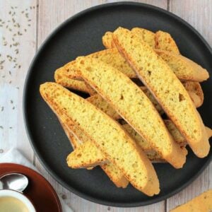 Anise seed biscotti piled on plate next to coffee cup.