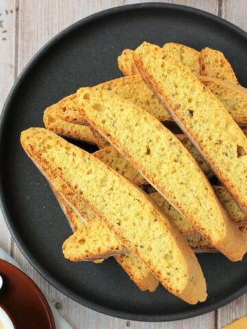 Anise seed biscotti piled on plate next to coffee cup.