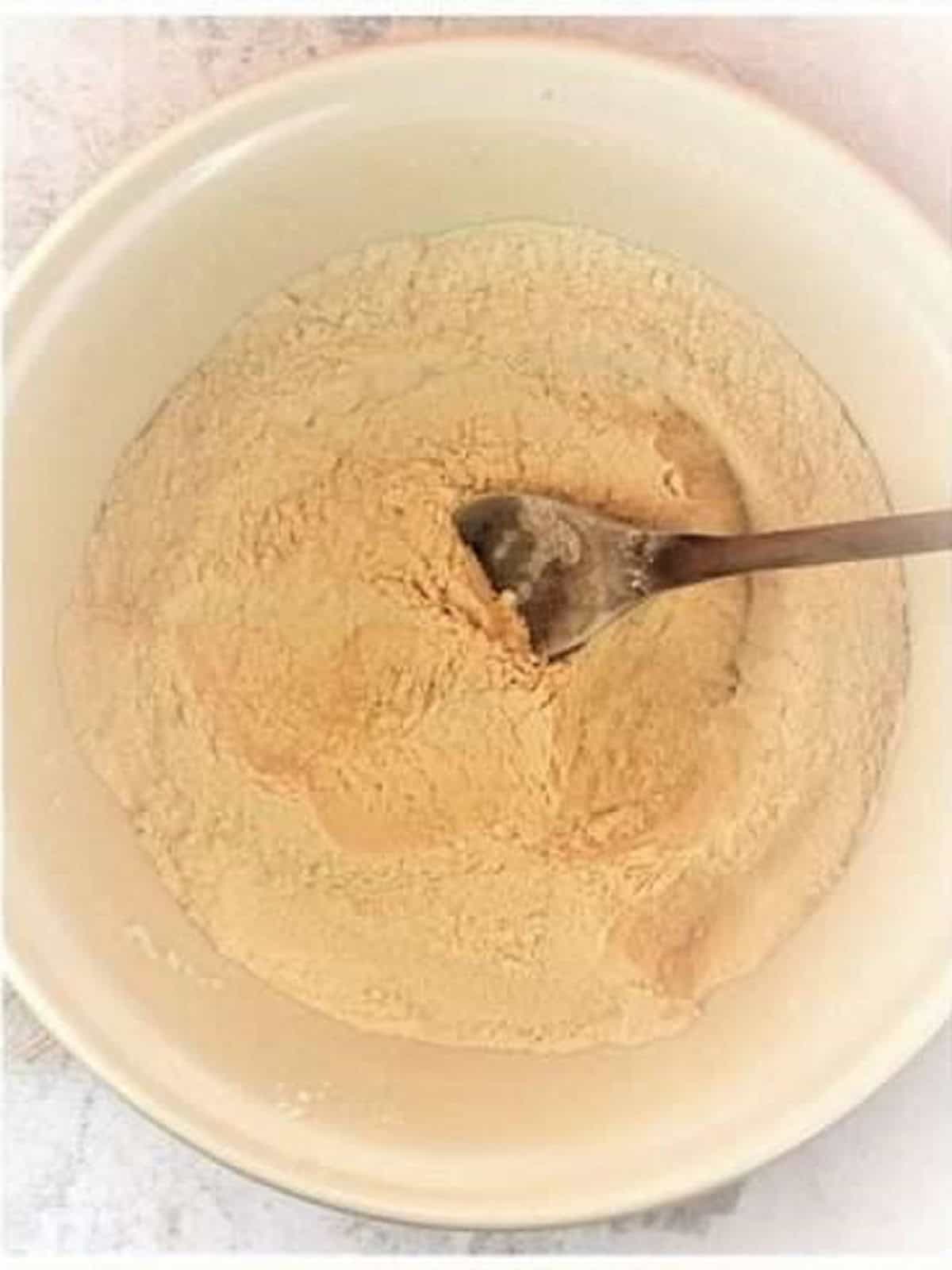 Dry ingredients blended with butter in mixing bowl with wood spoon.