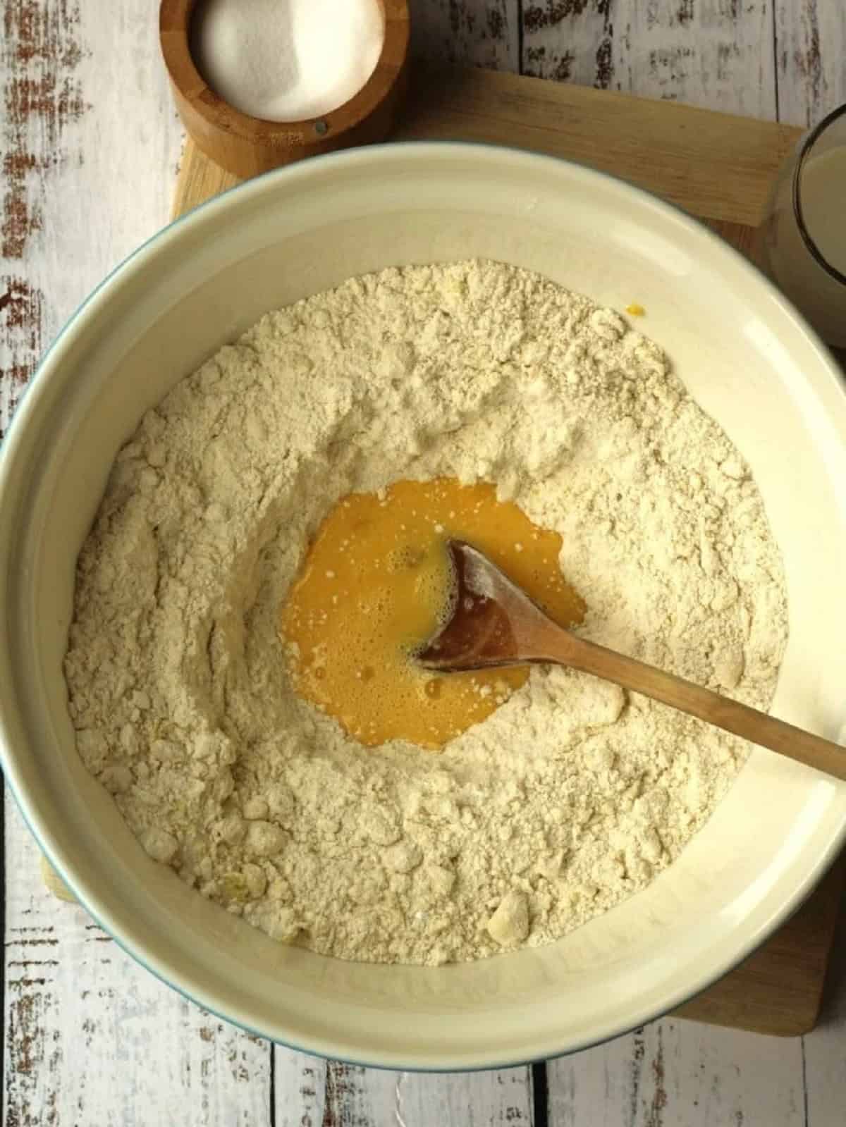 Beaten egg added to dry ingrdients in mixing bowl with wooden spoon.