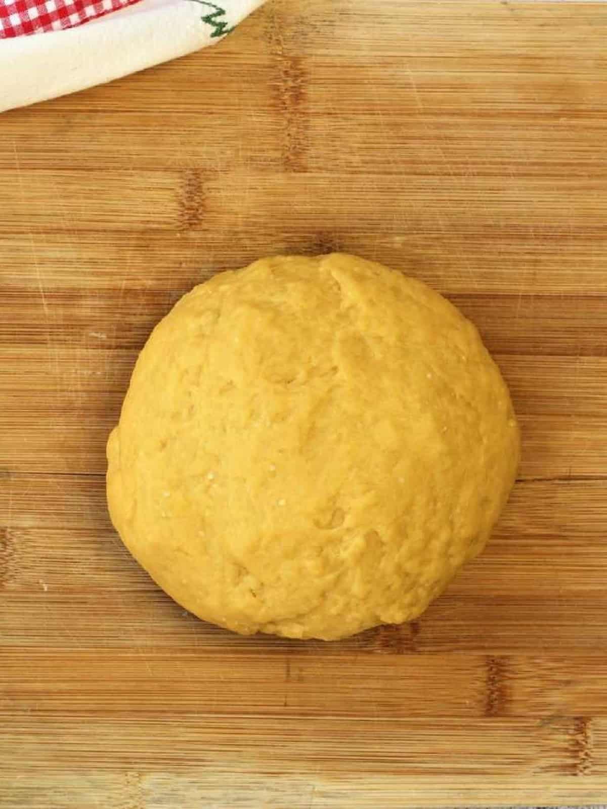 Pignolata dough shaped into a ball on wood board.