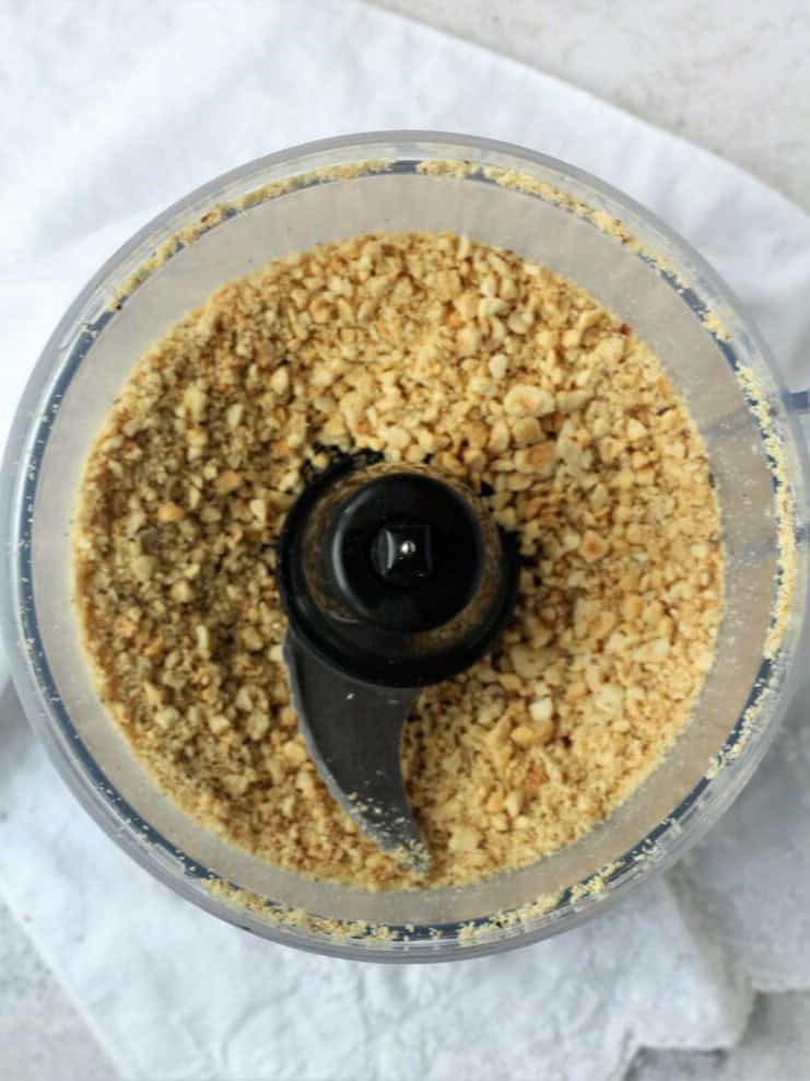 Coarsely ground hazelnuts in bowl of food processor.