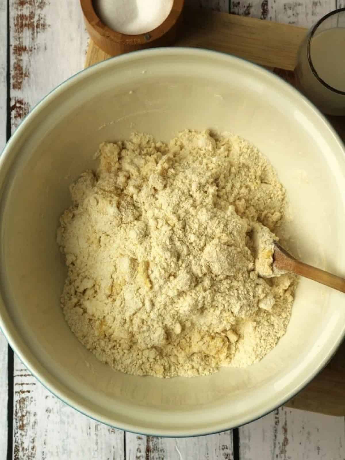 Raggedy dough for S cookies stirred in mixing bowl with wood spoon.
