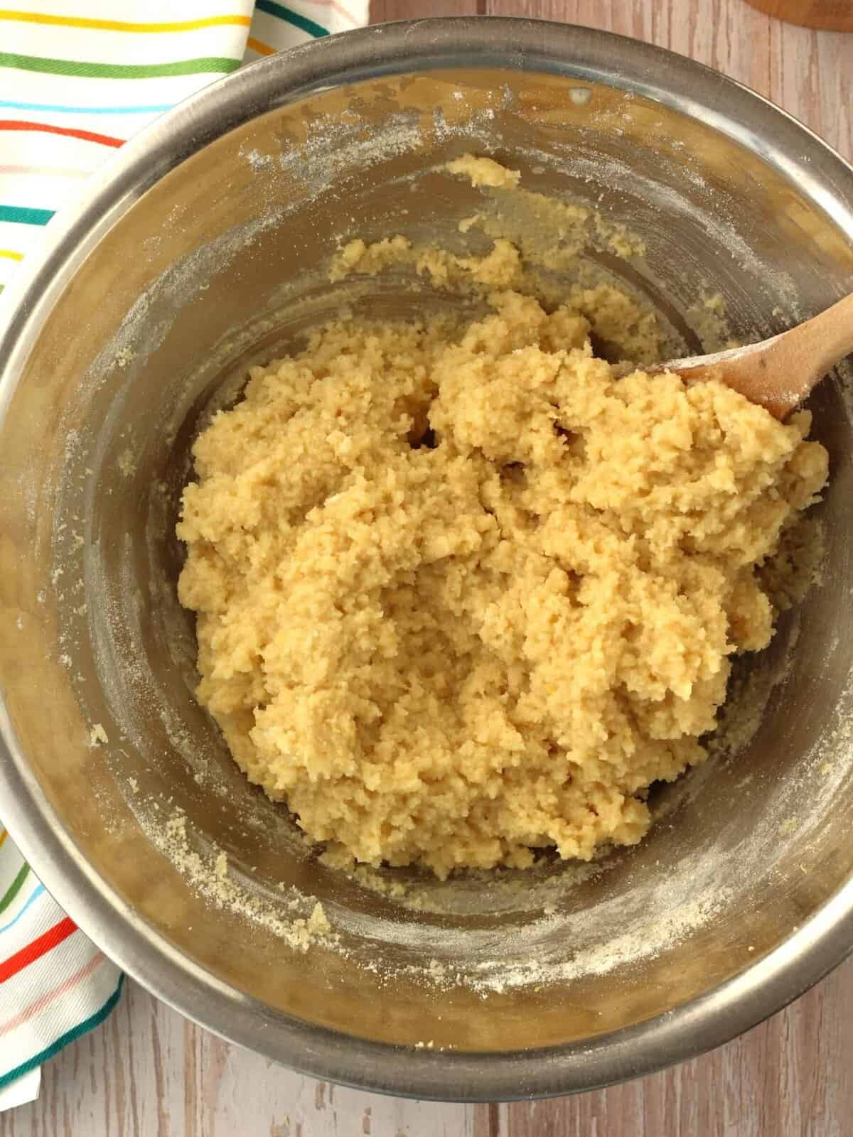 Lemon almond cookie dough in bowl with wooden spoon.