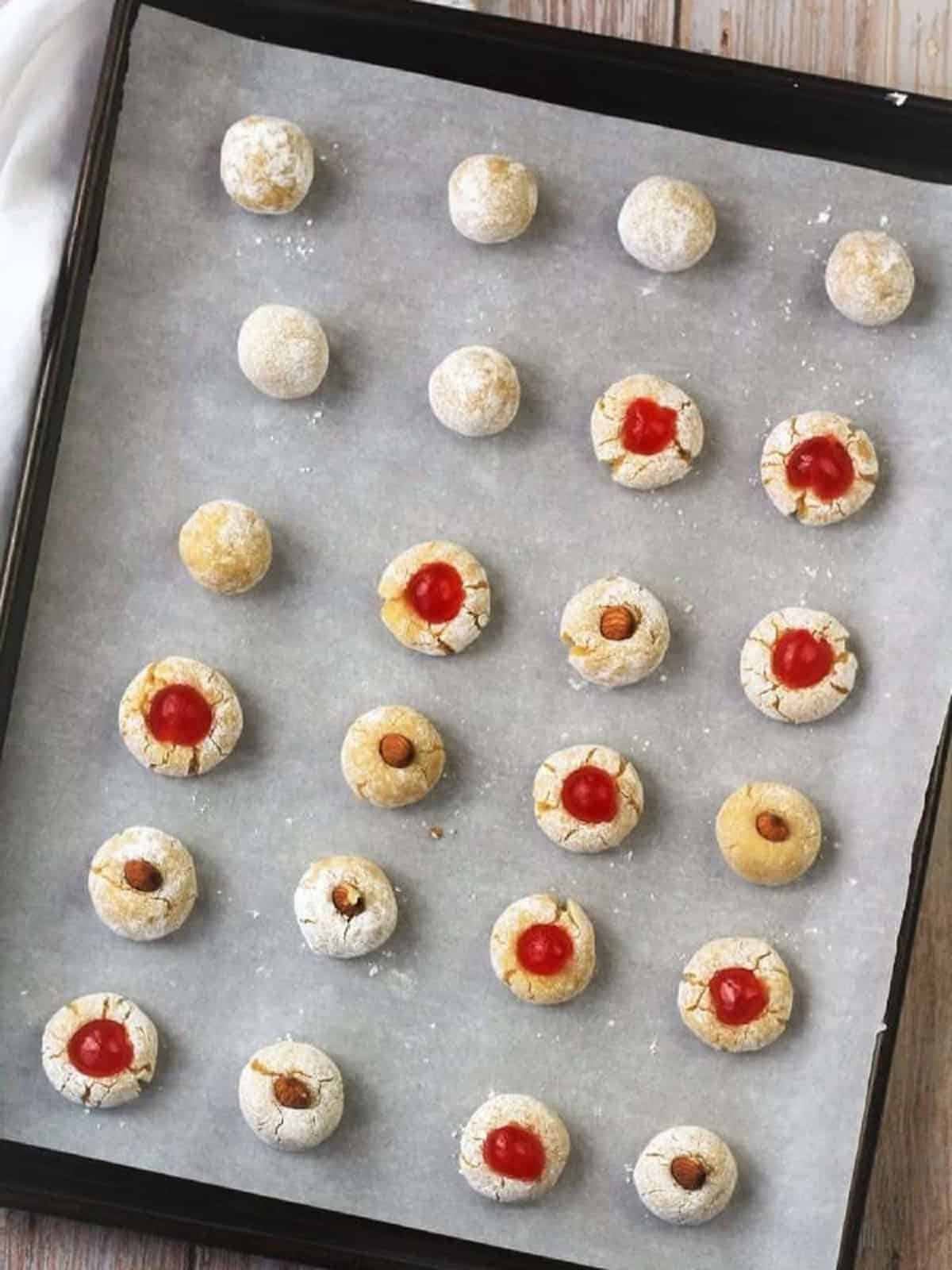 Amaretti cookie dough balls topped with cherries or almonds on baking sheet.