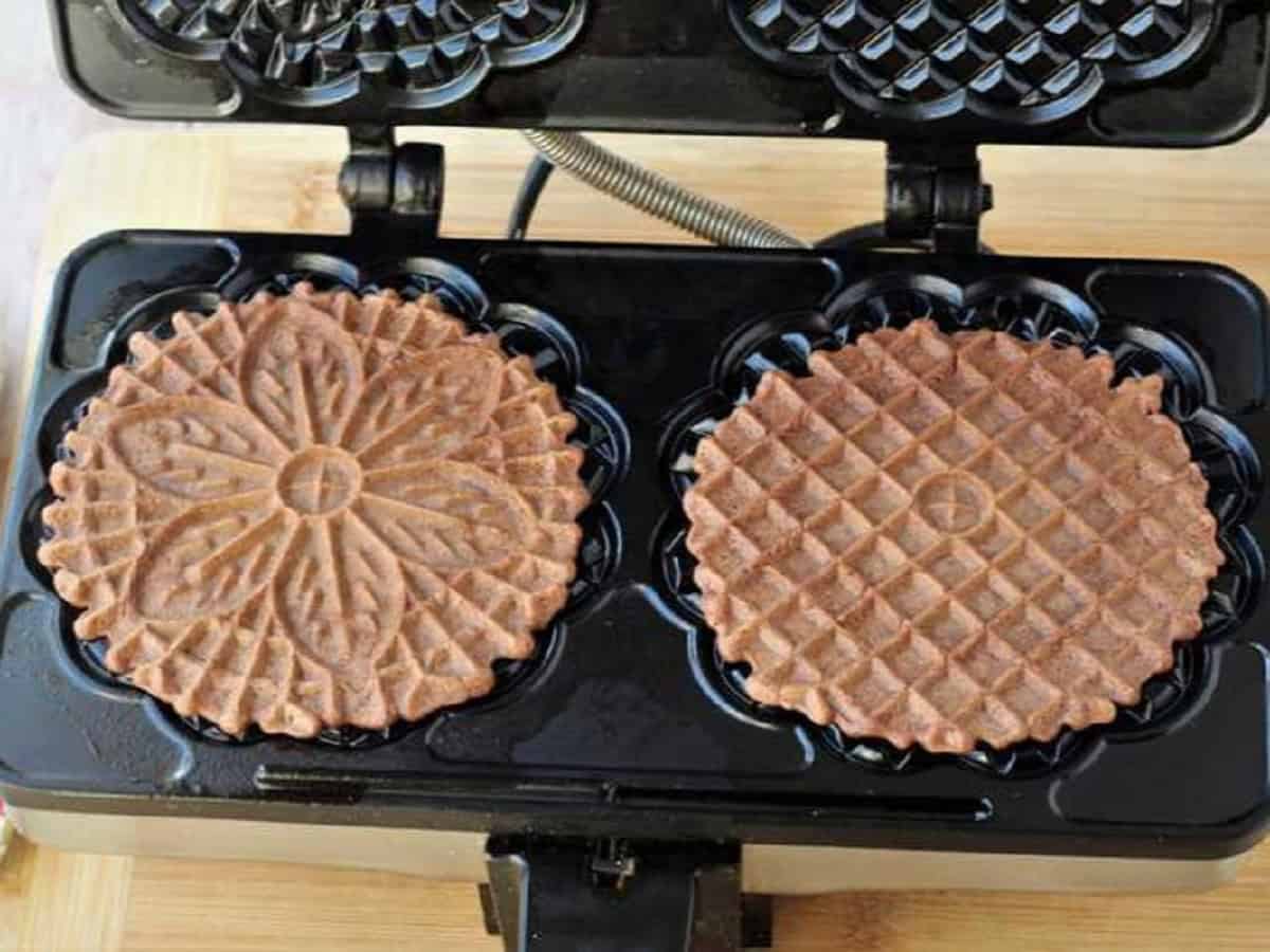Chocolate pizzelle cookies on iron pizzelle maker.