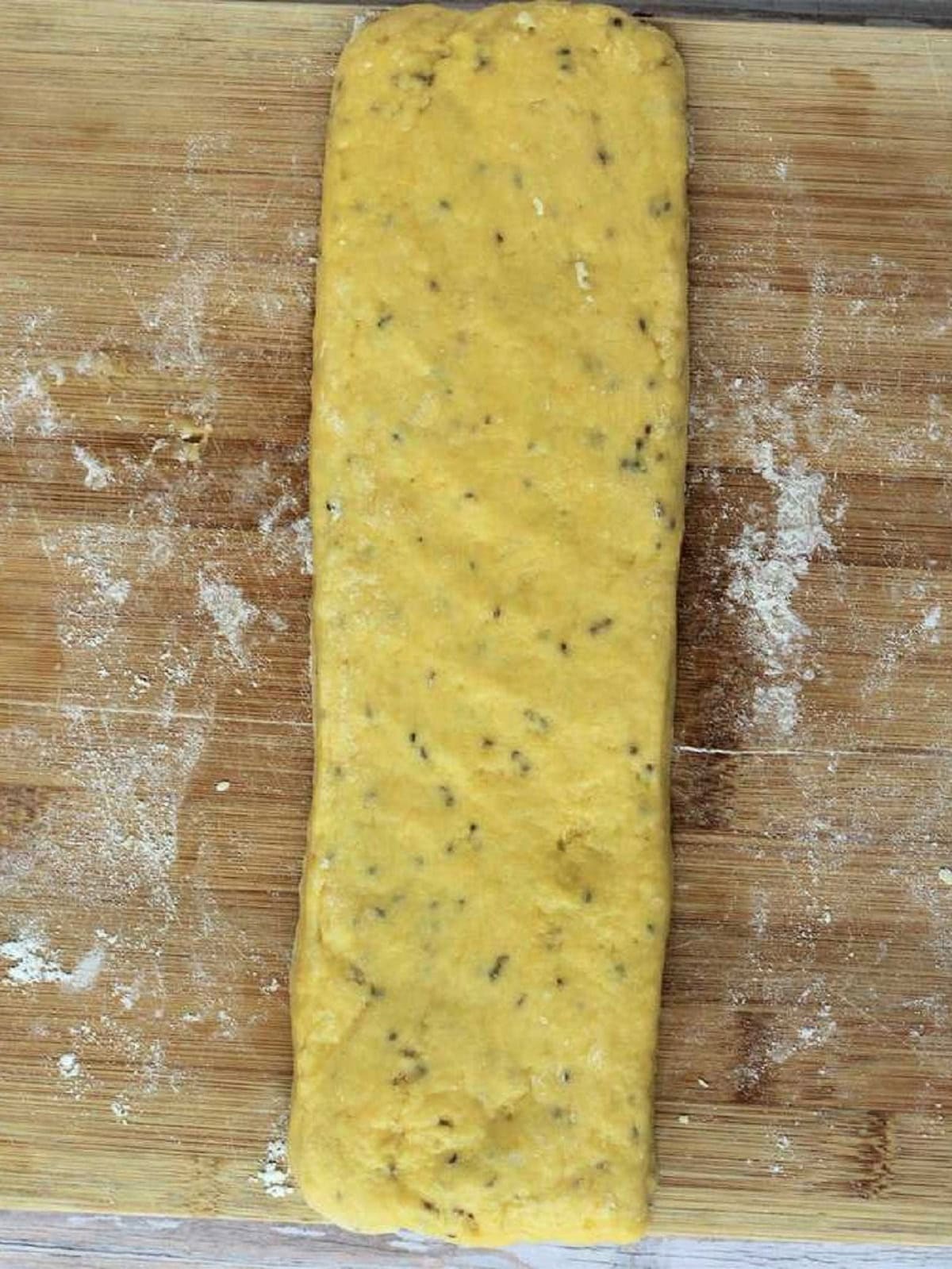 Anise biscotti dough shaped into long rectangle on wood board.