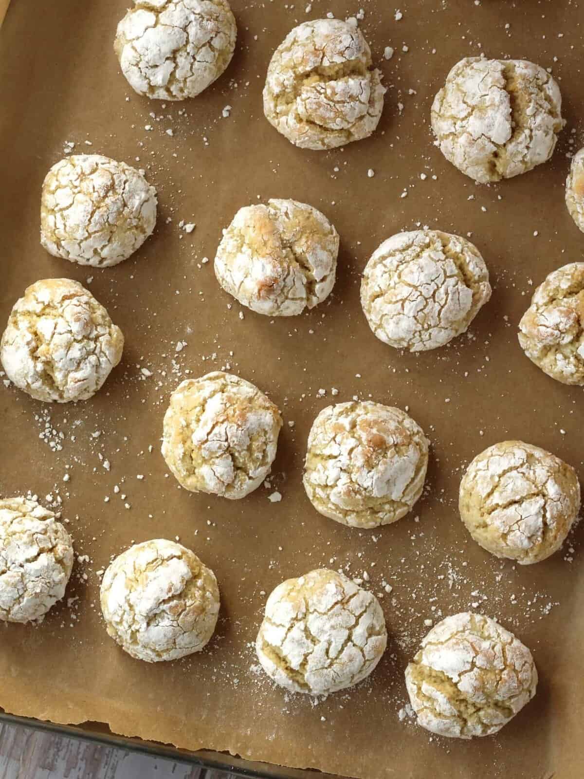 Lemon almond cookie balls rolled in powdered sugar on baking sheet.