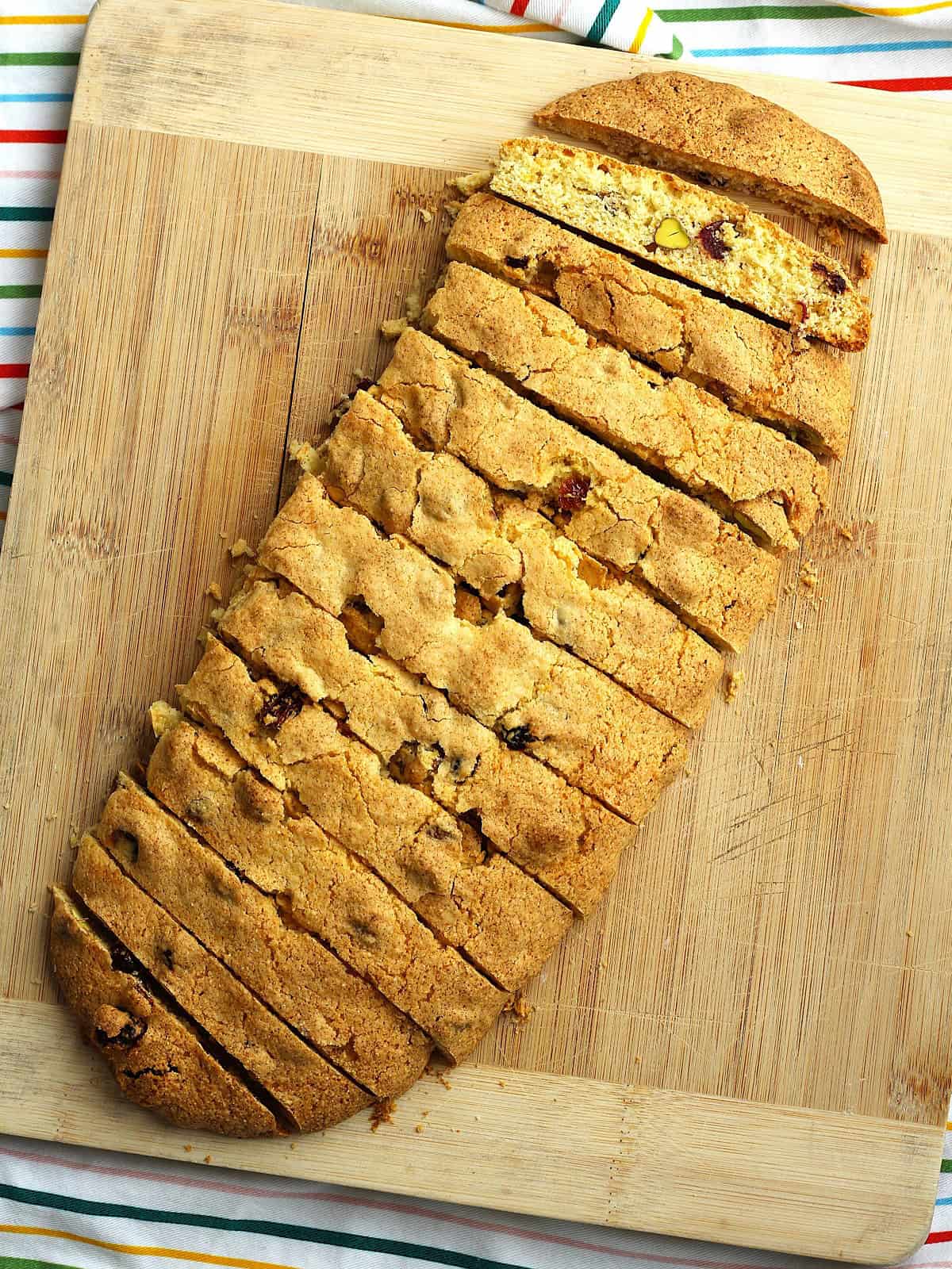 Sliced pistachio cranberry cornmeal biscotti on wood cutting board.