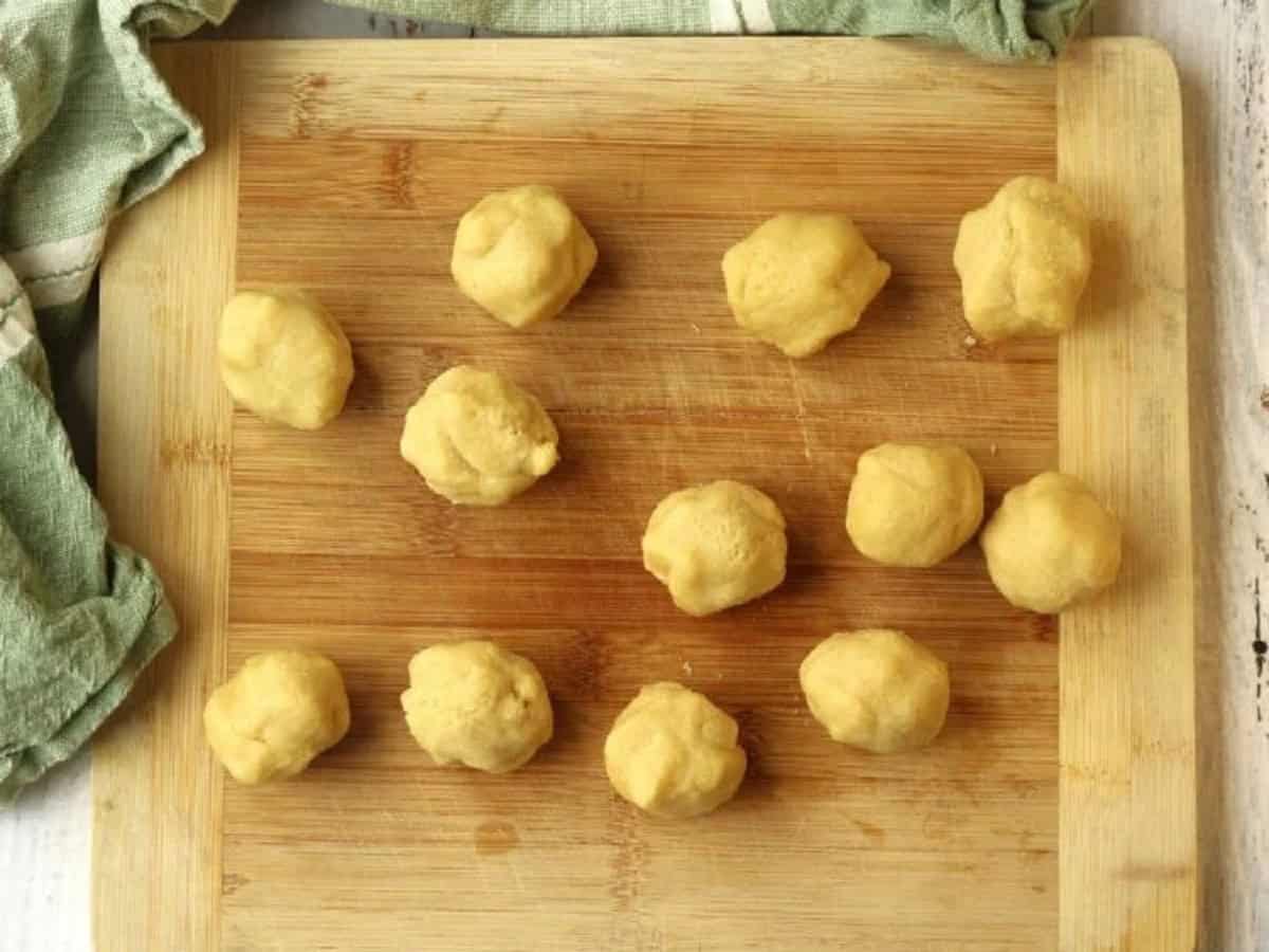 S-cookie dough shaped into balls on wood board.