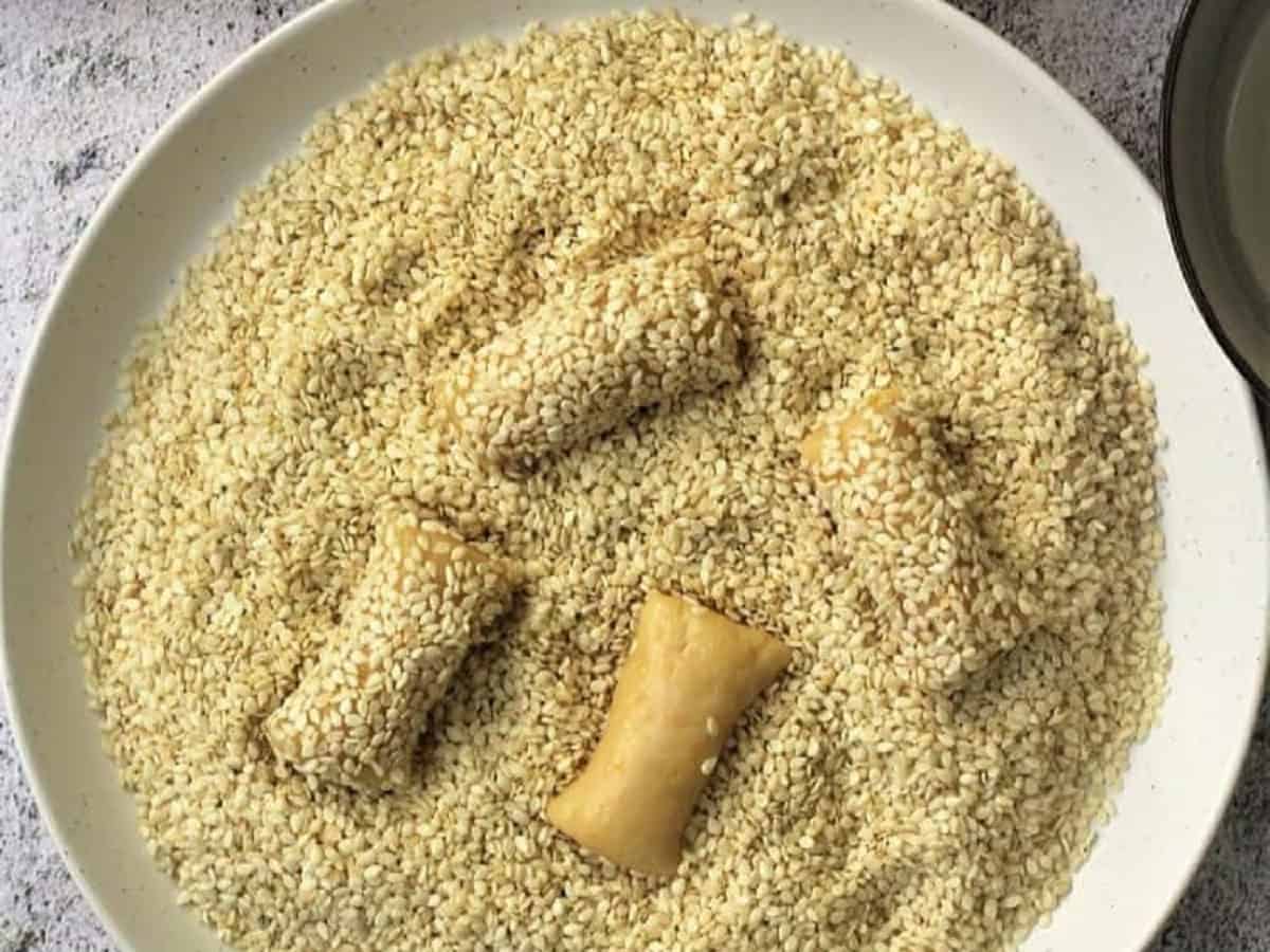 Sesame seed cookies dredged into plate with sesame seeds.