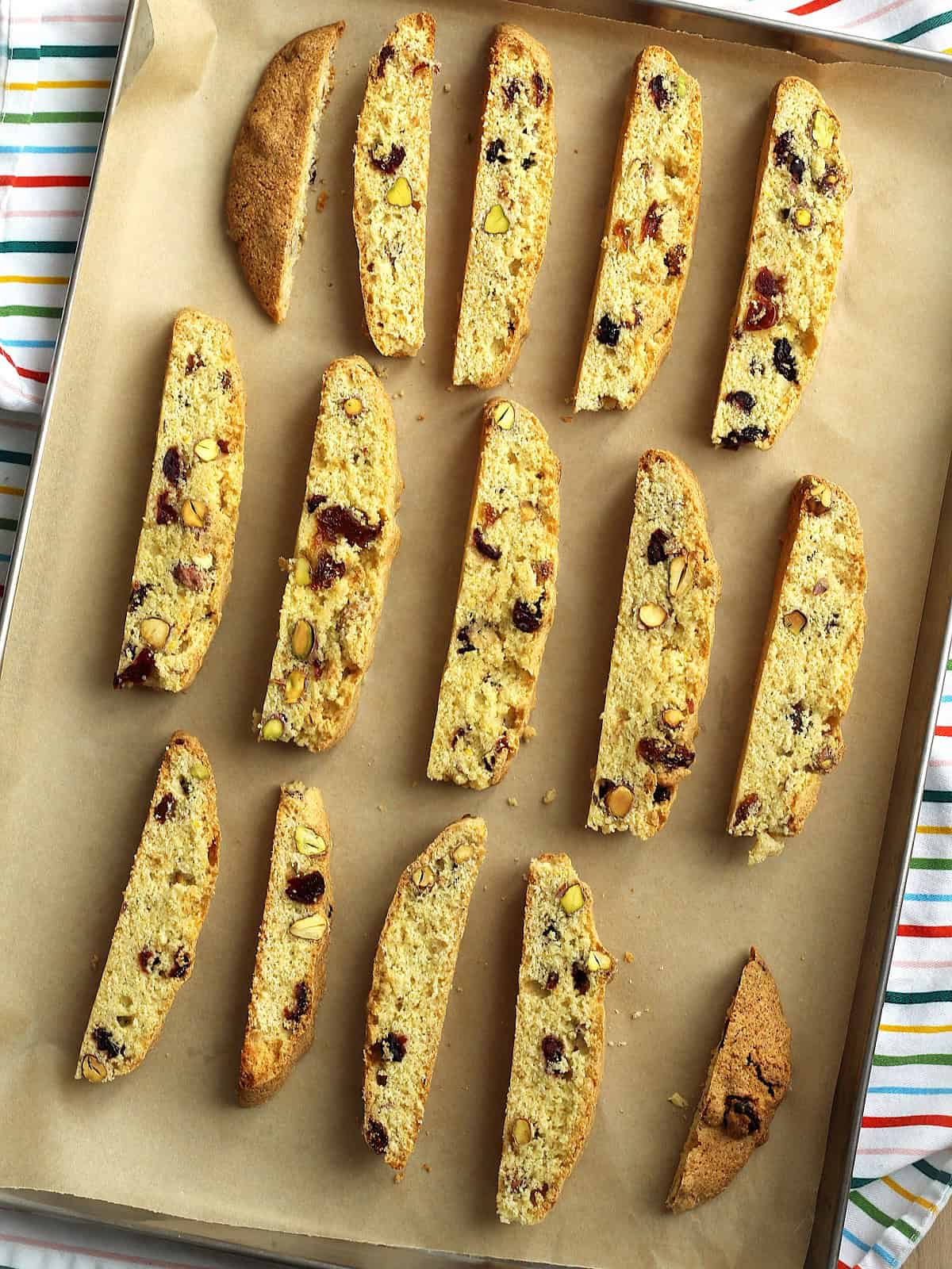 Sliced cornmeal biscotti with pistachios and cranberries on baking sheet.