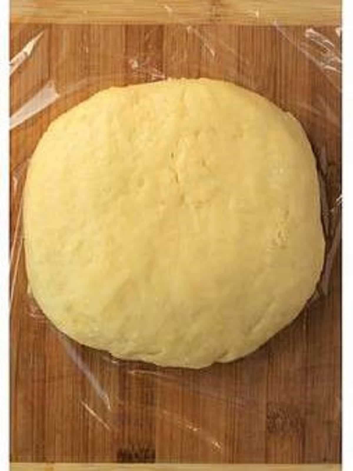 Cookie dough shaped into a disc on plastic wrap.