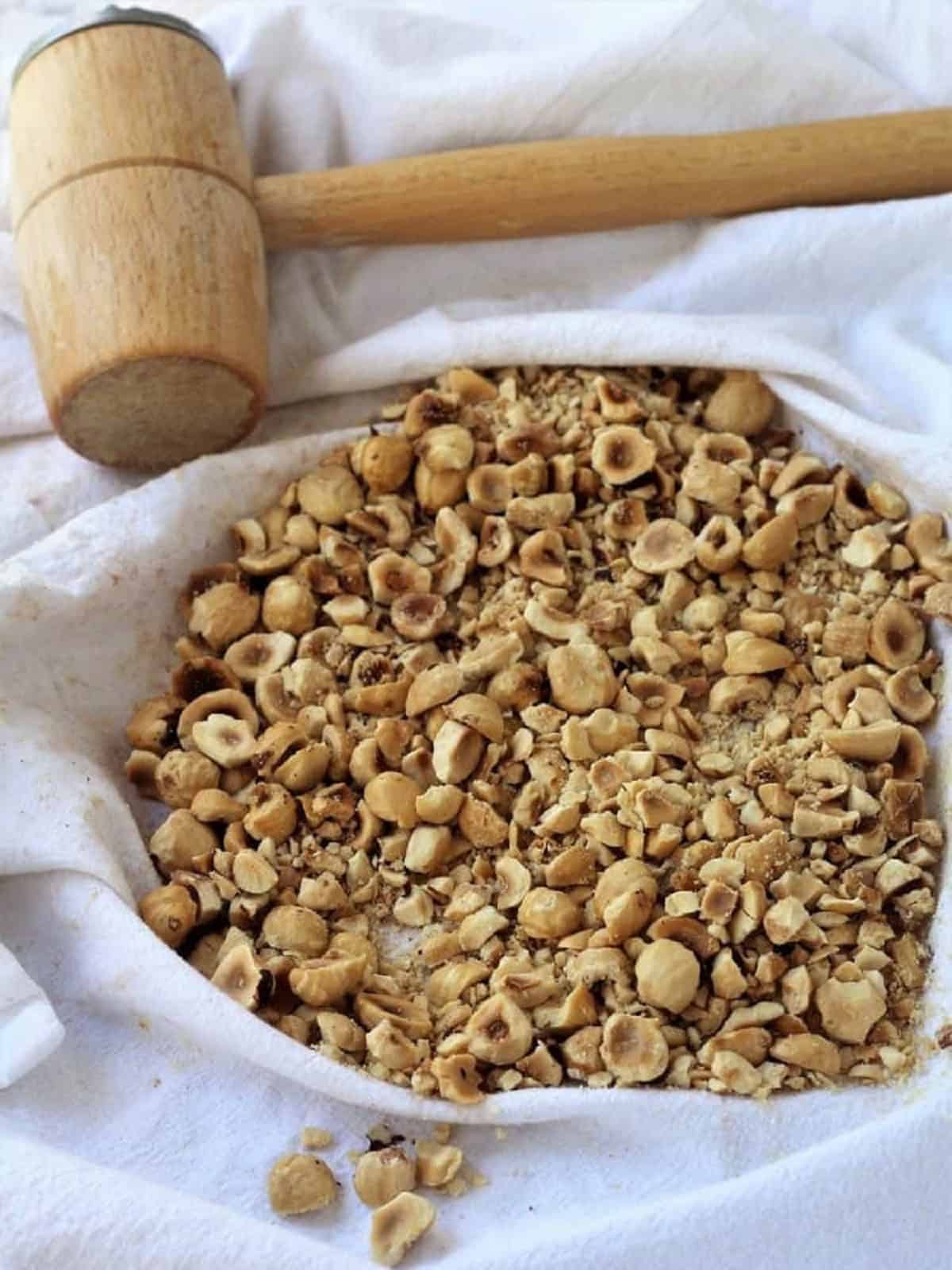 Chopped hazelnuts on dish cloth with meat mallet.