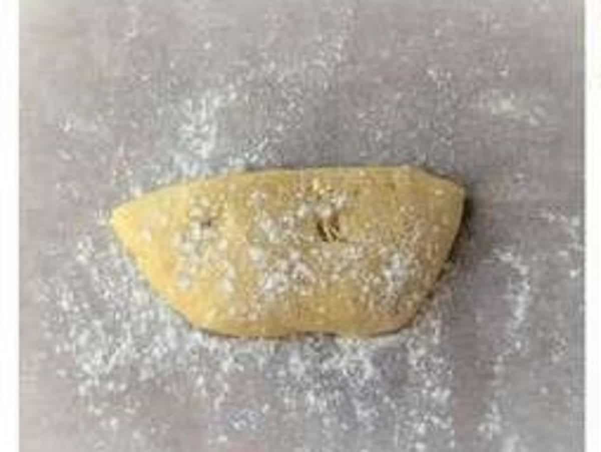 Nut and jam cookie dough half on parchment paper dusted with flour.