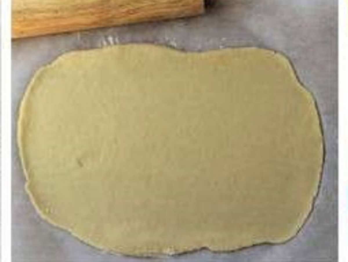 Shortcrust cookie dough rolled into rectangle with rolling pin.