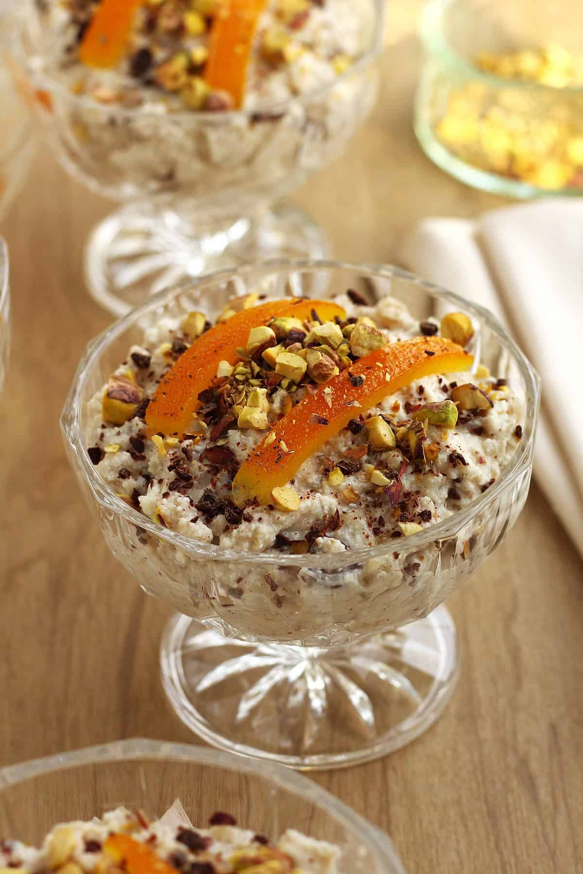 Sicilian ricotta dessert with wheat berries topped with candied orange peel and pistachios in glass cup.