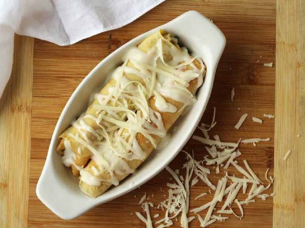Seafood filled crepes topped with cheese in baking dish.