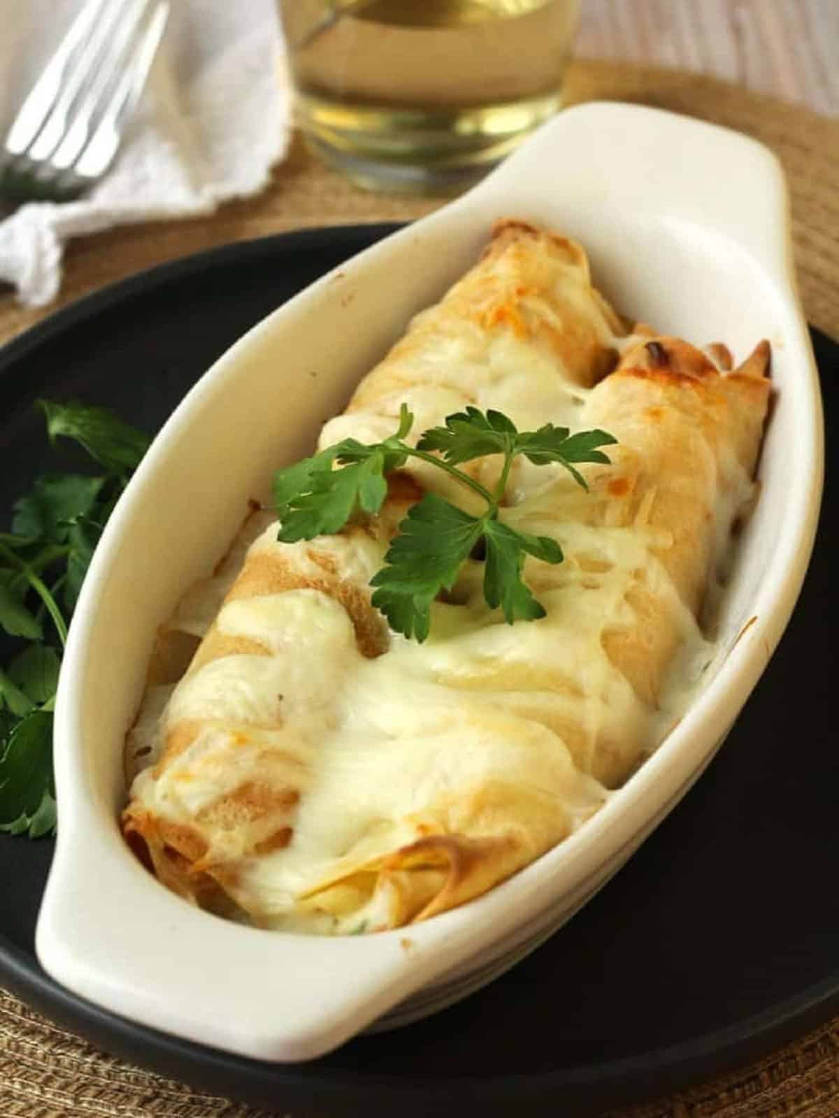 Seafood crepes topped with cheese baked in casserole dish.
