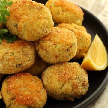 Crispy baked breaded potato and cod croquettes piled on plate with lemon wedge.
