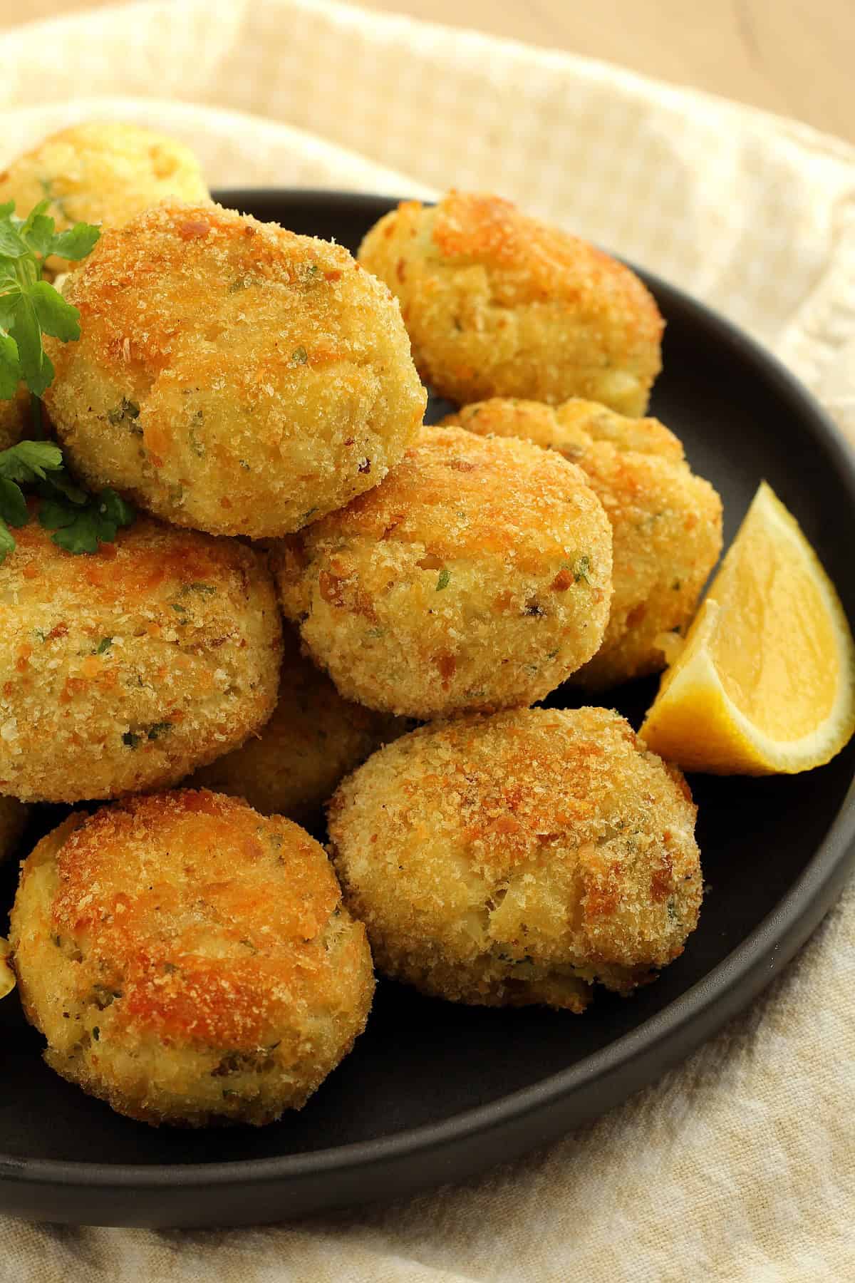 Crispy baked breaded potato and cod croquettes piled on plate with lemon wedge.