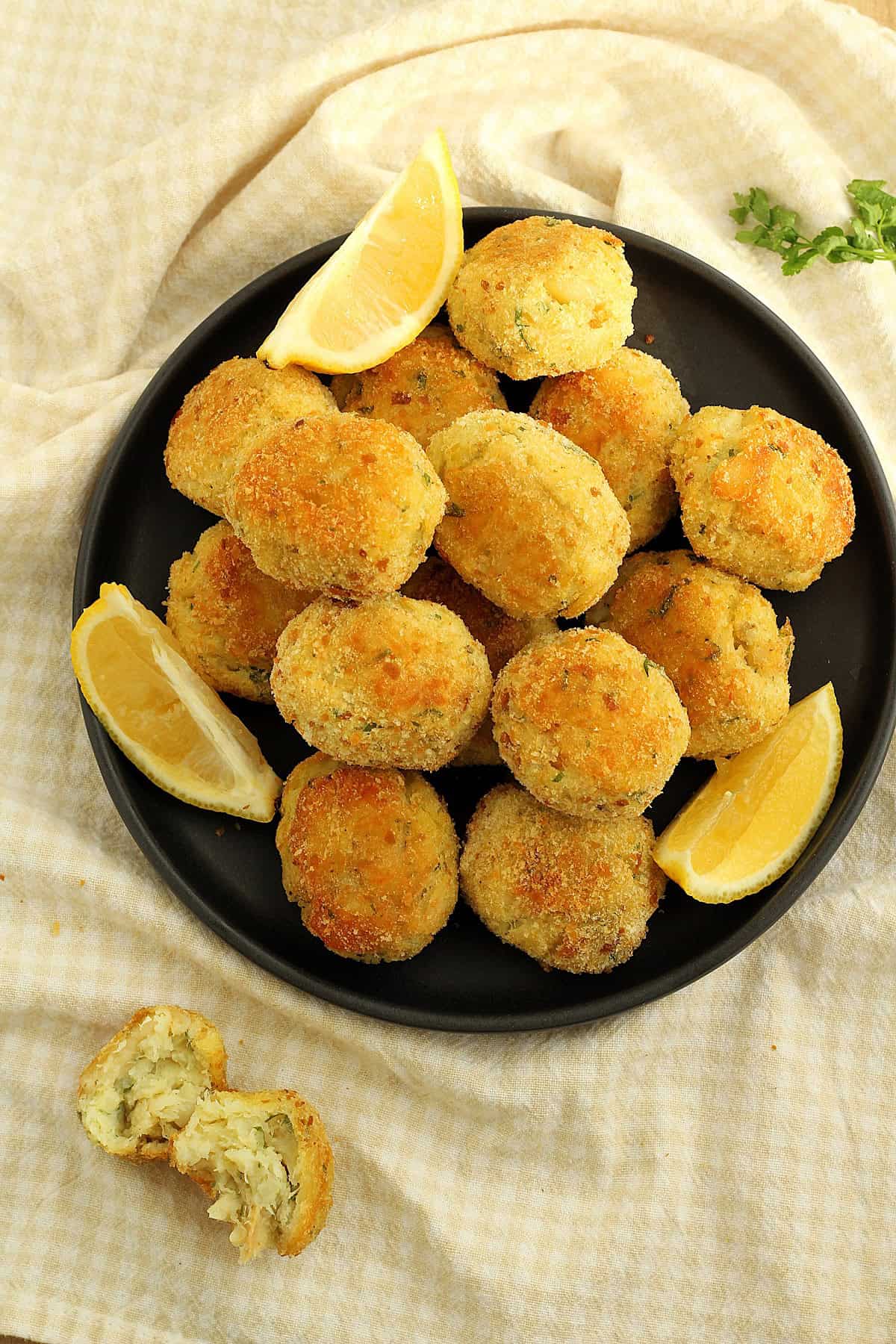 Cod and potato croquettes piled on plate with lemon wedges and parsley sprig on side.