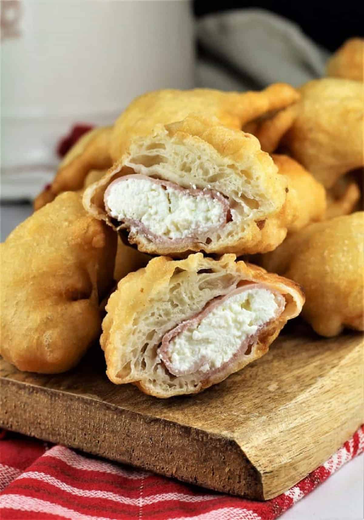 Sfingi stuffed with ricotta and prosciutto cotto cut in half on wood board.