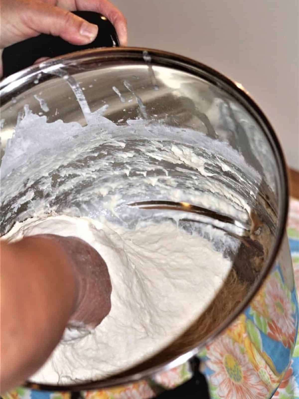 Stirring sfinci dough by hand in circular motions in large pot.