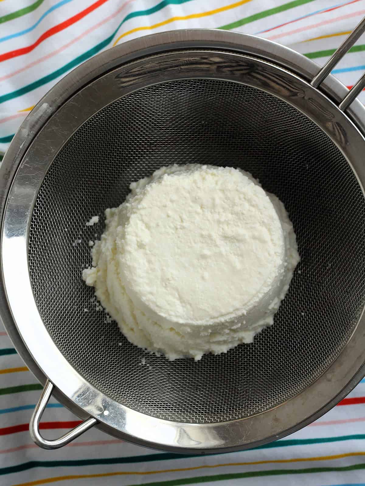 Ricotta placed in a sieve over a bowl to drain excess liquid.