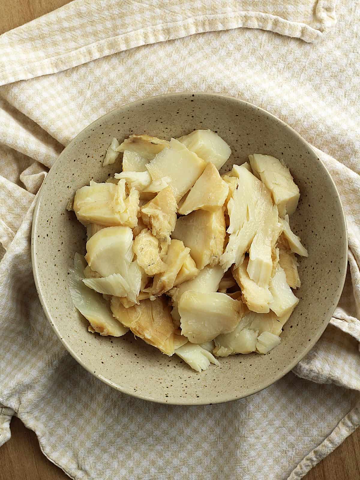 Boiled salt cod broken into small pieces in bowl.