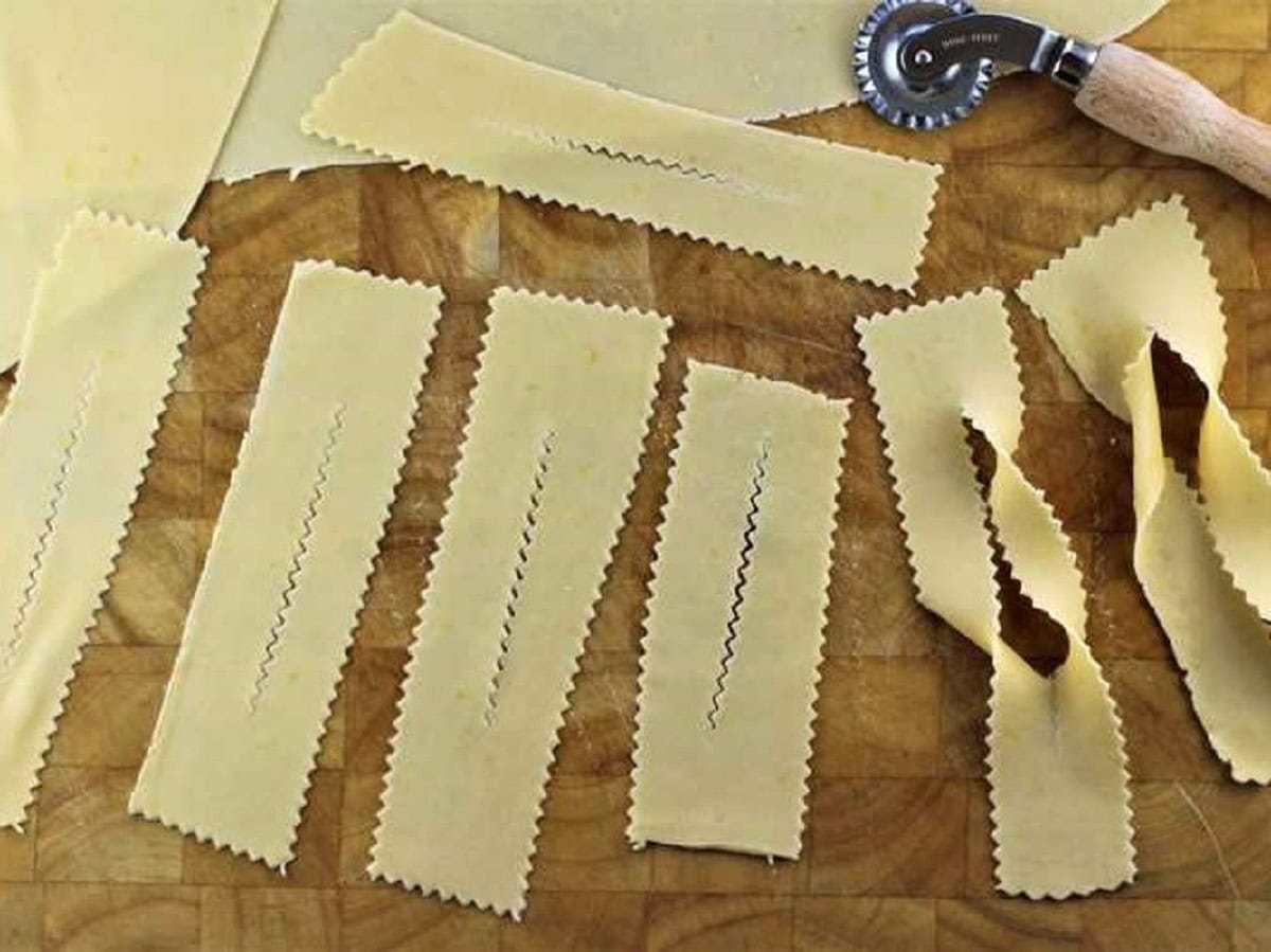 Strips of dough cut to shape chiacchiere with ravioli cutter wheel.