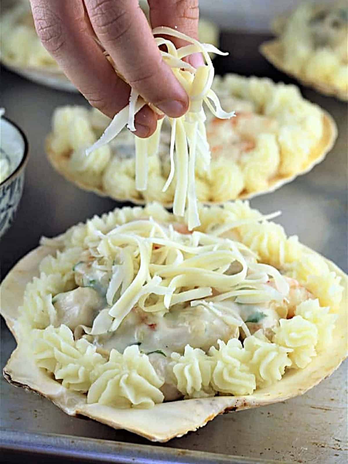 Sprinkling shredded cheese on coquilles St-Jacques, scallop shells filled with seafood.