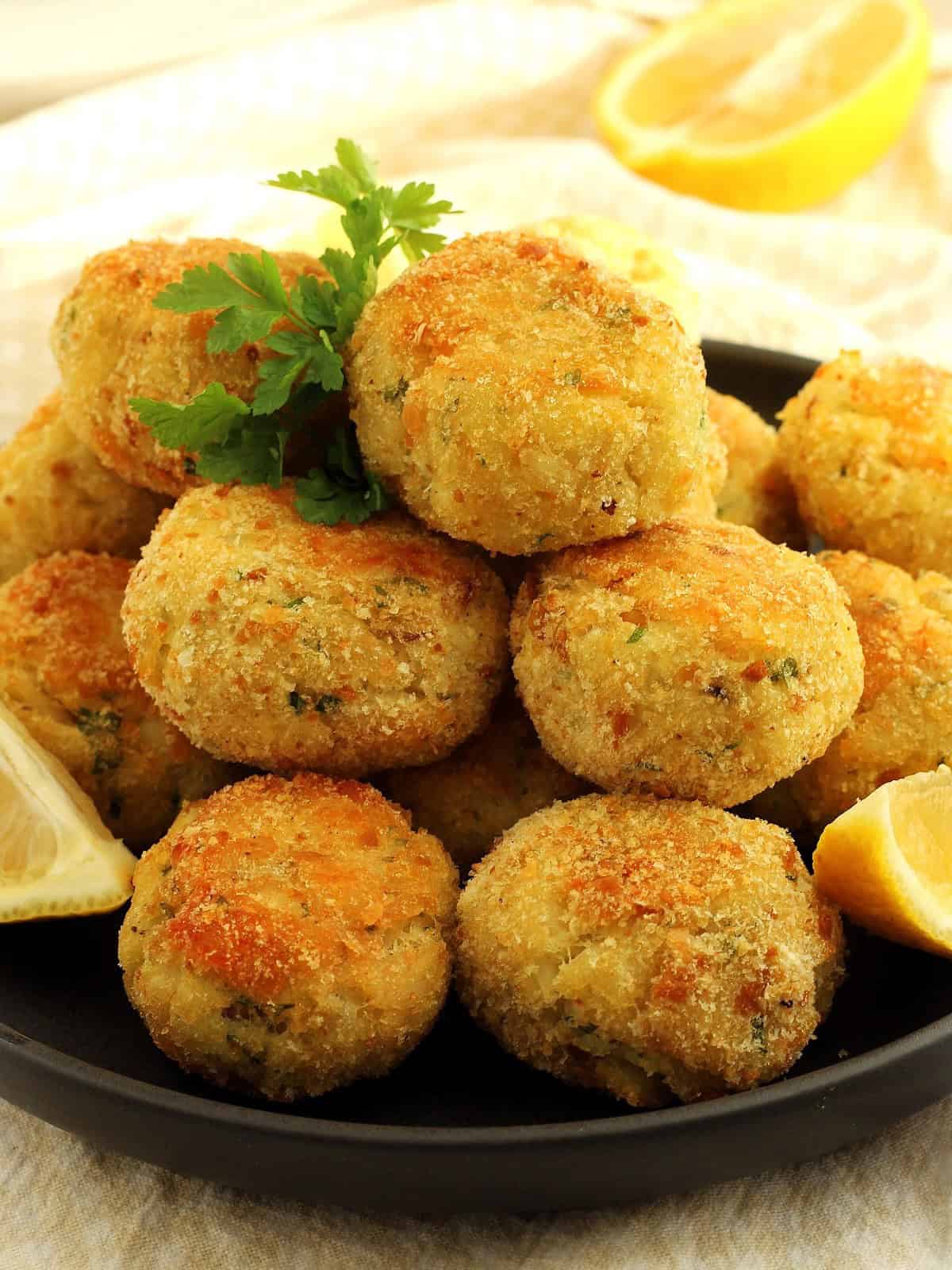 Potato and codfish croquettes piled on plate with lemon wedges and parsley sprig.