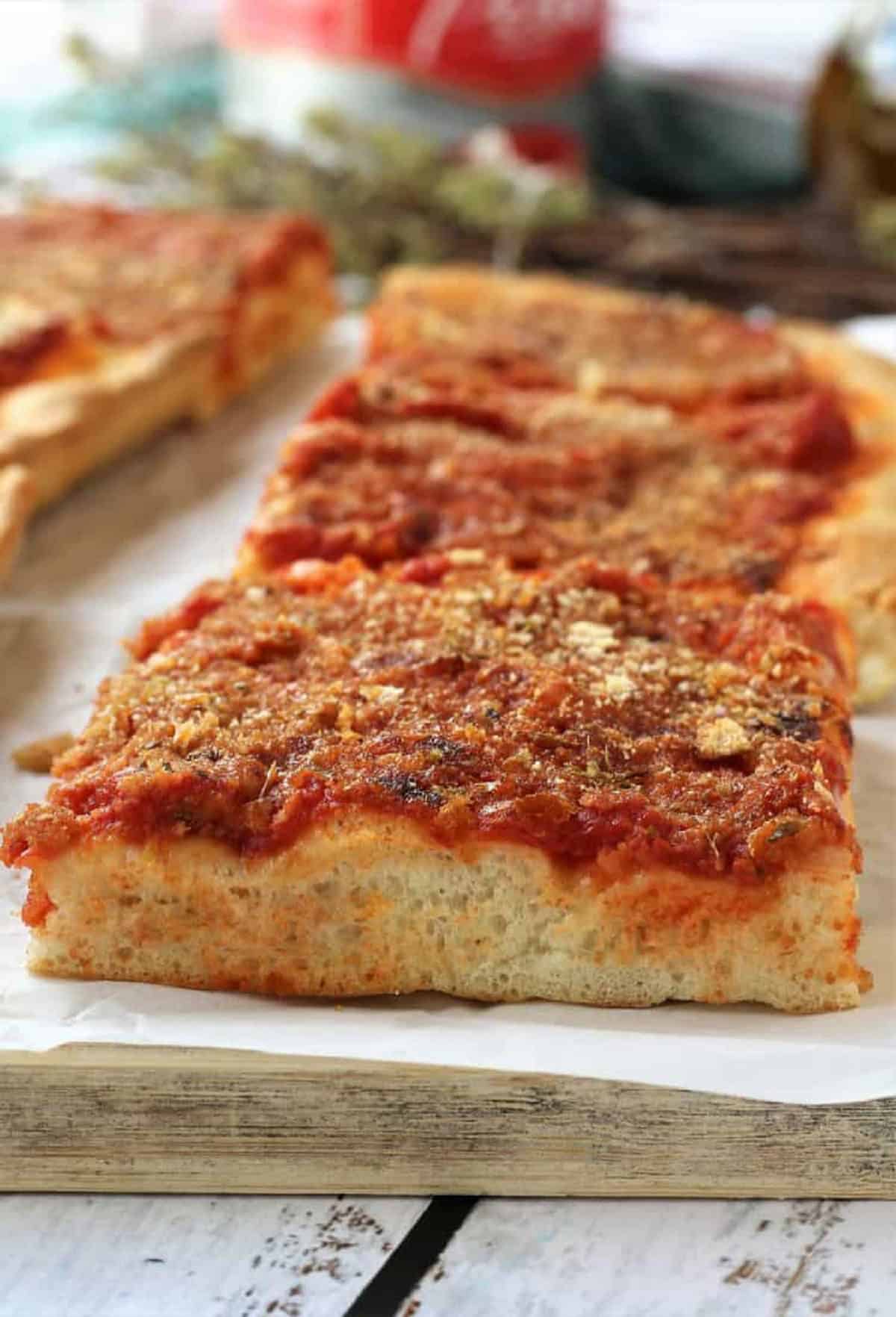 Sfincione Siciliano (Sicilian Style Pizza) Sfincione siciliano, Sicilian style pizza, cut into squares on wood board.