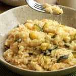 Creamy zucchini risotto with scamorza cheese scooped up with fork leaving cheese strings behind.