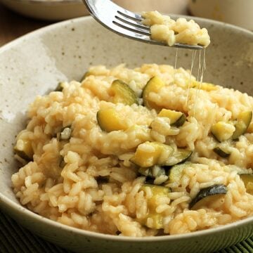 Creamy zucchini risotto with scamorza cheese scooped up with fork leaving cheese strings behind.