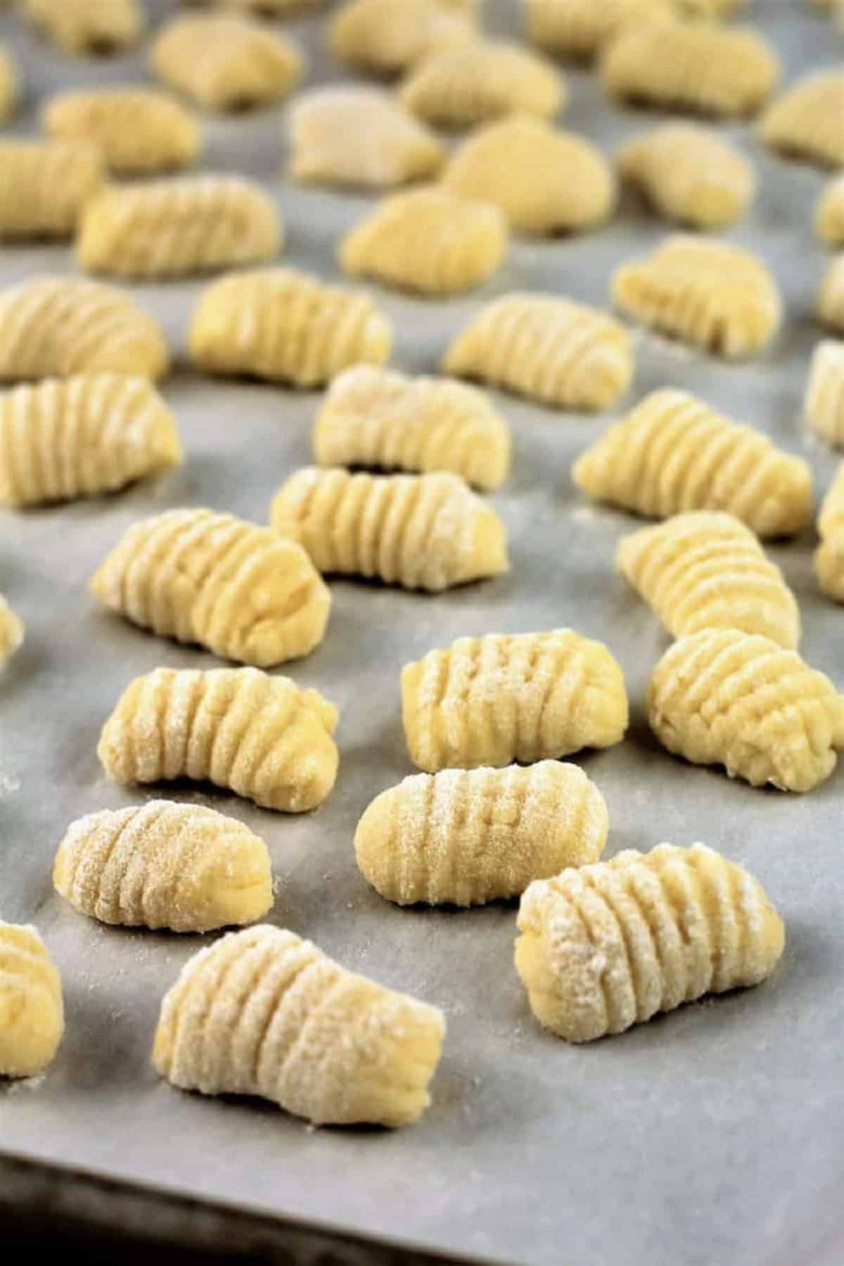 Ricotta gnocchi resting on parchment covered baking sheet.