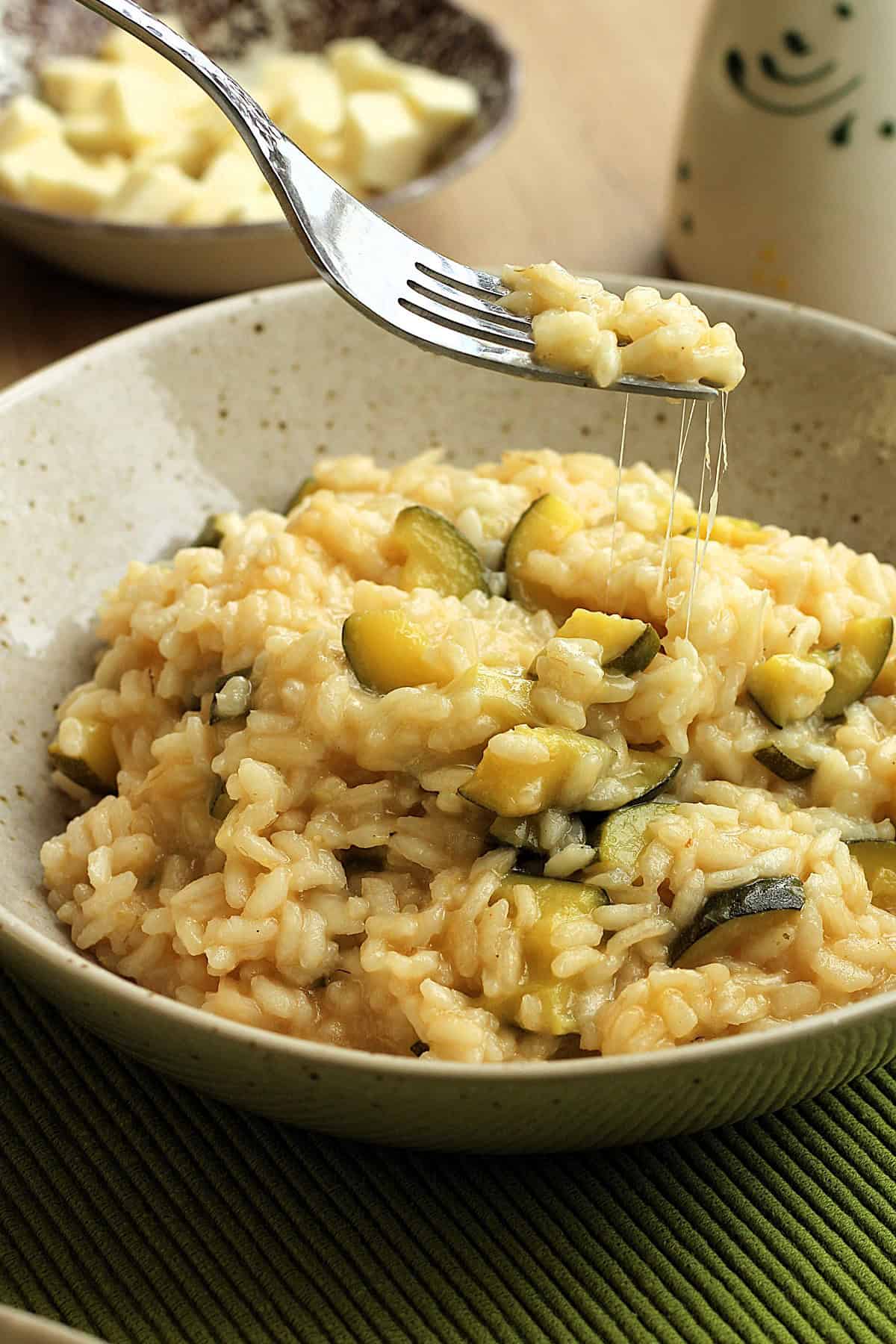 Creamy zucchini risotto with scamorza cheese scooped up with fork leaving cheese strings behind.