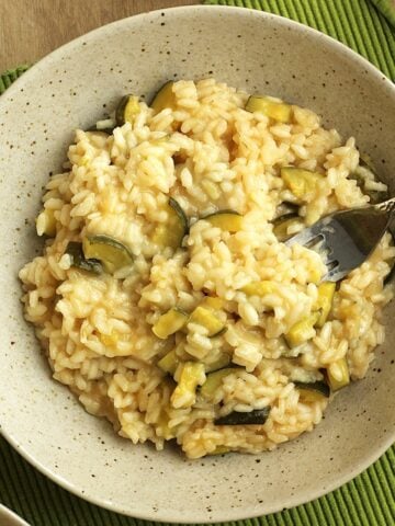 Risotto with zucchini and scamorza cheese in bowl with fork in it.