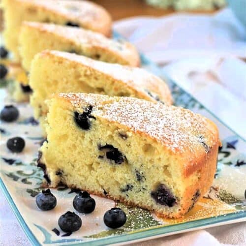 Slices of olive oil cake with blueberries on serving plate with blueberries around it.