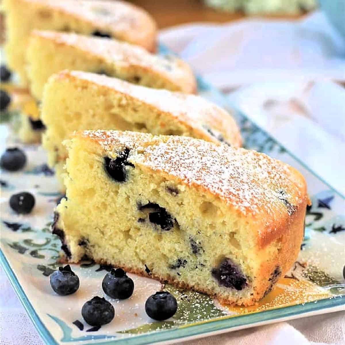 Slices of olive oil cake with blueberries on serving plate with blueberries around it.