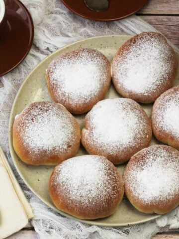 Baked Sicilian iris with ricotta filling on plate next to coffee cups.