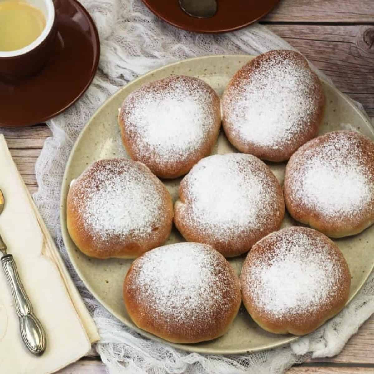 Baked Sicilian iris with ricotta filling on plate next to coffee cups.